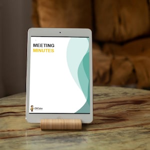 May include: A white tablet displaying a document titled "MEETING MINUTES" in yellow text, supported by a wooden stand. The document has a teal and white design. The tablet rests on a brown, patterned table.