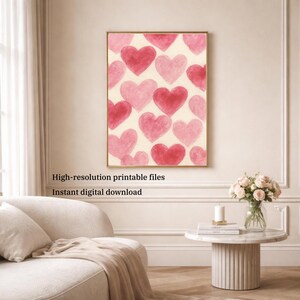 May include: A framed print featuring a pattern of pink and red watercolor hearts on a cream background. The artwork is displayed in a gold frame. Text at the bottom reads: "High-resolution printable files" and "Instant digital download."