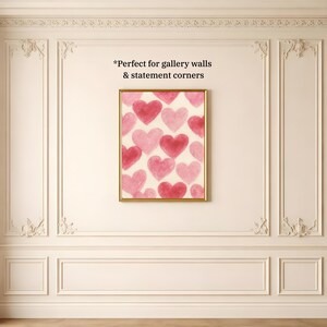 May include: A framed artwork featuring a pattern of pink and red hearts on a cream background. The artwork is in a gold frame and hangs on a white wall with decorative molding. The text "Perfect for gallery walls & statement corners" is visible.