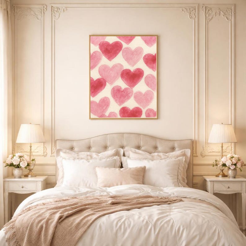 May include: A framed artwork featuring a pattern of watercolor hearts in shades of pink and red against a cream background. The artwork is displayed above a bed with white bedding and a blush-colored throw.