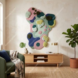 May include: Abstract wall art rug in a unique shape, featuring a mix of colors including pink, blue, green, and yellow. The rug is mounted on a neutral-colored wall, creating a focal point in a modern living space. The rug is labeled with the text "MUSKAN CARPET".