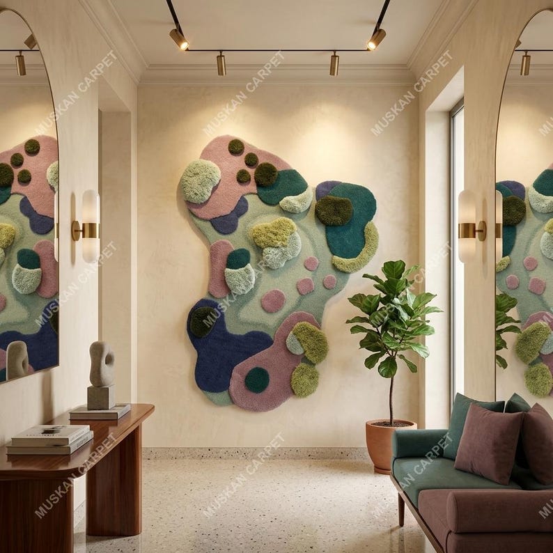 May include: Abstract wall art rug in shades of pink, blue, green, and purple. The rug has an irregular shape with textured elements. The words "MUSKAN CARPET" are printed on the wall. The room features a sofa, a plant, and a wooden table.
