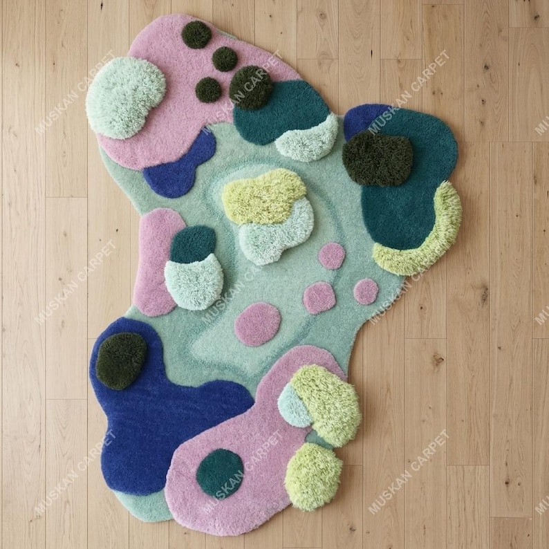 May include: Abstract-shaped rug with a pastel color palette. The rug features a light green base with pink, blue, and yellow organic shapes. Some shapes have a textured, raised appearance. The rug is on a wooden floor.