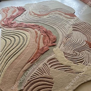 May include: A large, abstract area rug with a flowing, organic design. The rug features a mix of colors, including shades of beige, pink, and brown, with a textured, carved appearance. The design resembles a landscape or geological formation.