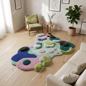 May include: A colorful, abstract area rug with a unique, organic shape. The rug features a combination of blue, pink, green, and olive-green tufted sections. The rug is placed on a hardwood floor, with a sofa and chair in the background.