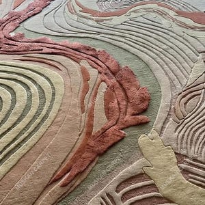May include: A close-up of a rug with an abstract design. The rug features a blend of colors, including shades of pink, beige, and green, arranged in flowing, wave-like patterns. The texture appears soft and plush, with a detailed, carved effect.