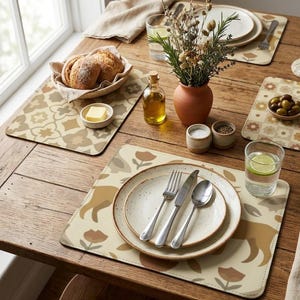 May include: A rustic dining table setting with patterned placemats, plates, silverware, and a vase of dried flowers. The table is set with bread, butter, olive oil, salt, pepper, and drinks. The placemats have a floral design.