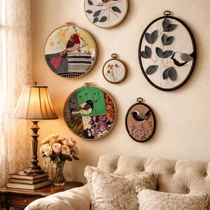 Puede incluir: Una colección de bordados enmarcados con diseños de aves y flores. Las obras de arte se exhiben en una pared beige sobre un sofá. Los aros de bordado son redondos y ovalados, con varios fondos de tela e ilustraciones de aves.