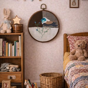 May include: A circular textile artwork featuring a bird design is displayed above a child's bed. The artwork depicts a bird with blue and brown feathers, and blue flowers. The room is decorated with a wooden bookshelf, a toy horse, and a teddy bear.