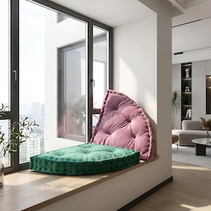 Peut inclure: Un coin de fenêtre avec deux coussins moelleux. L'un, en forme de triangle arrondi, est rose poudré, l'autre, carré, est vert foncé. Les coussins sont posés sur un rebord de fenêtre en bois.
