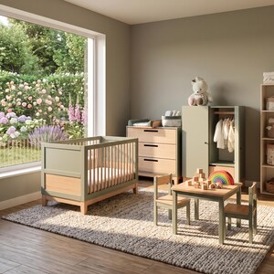 May include: A nursery room with sage green and natural wood furniture. The room includes a crib, dresser, wardrobe, small table, and chairs. A plush teddy bear sits atop the wardrobe. A large window offers a view of a garden.