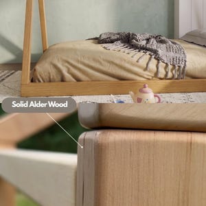 Puede incluir: Primer plano de muebles de madera maciza de aliso, que muestra la veta y la textura natural de la madera. La imagen destaca la artesan&iacute;a y la calidad de la estructura de la cama de madera y otras piezas de mobiliario. El texto "Solid Alder Wood" es visible.