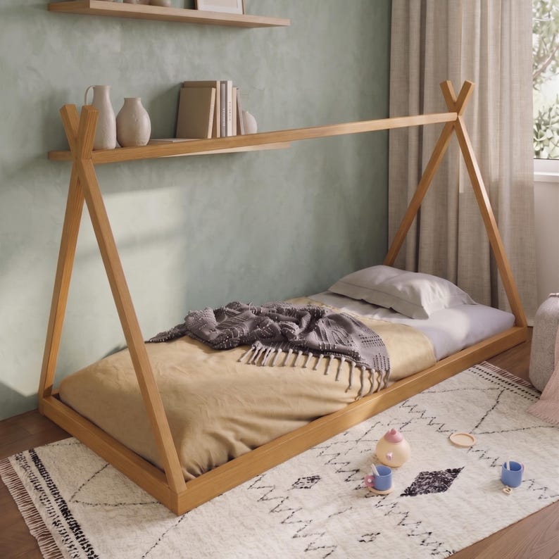 Puede incluir: Una cama de madera estilo tipi con un colch&oacute;n marr&oacute;n claro, una manta gris y una almohada blanca. La cama est&aacute; sobre una alfombra blanca con un patr&oacute;n geom&eacute;trico negro. Hay objetos decorativos en una estanter&iacute;a encima de la cama.