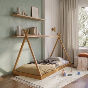 Puede incluir: Una cama de madera clara con forma de tipi, con un colch&oacute;n beige y una manta gris. La cama est&aacute; sobre una alfombra estampada en una habitaci&oacute;n con paredes verde claro y estantes de madera con objetos decorativos.