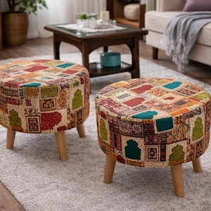 May include: Two round ottomans with a patchwork design in shades of red, orange, green, and teal. The ottomans have wooden legs and are placed on a light gray rug. The design features geometric and floral patterns.