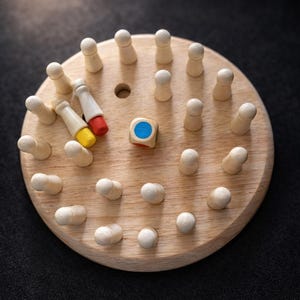 May include: Wooden board game with a circular wooden base, featuring small wooden pegs and colorful game pieces. A wooden die with a blue circle is in the center. The game is set against a dark background.