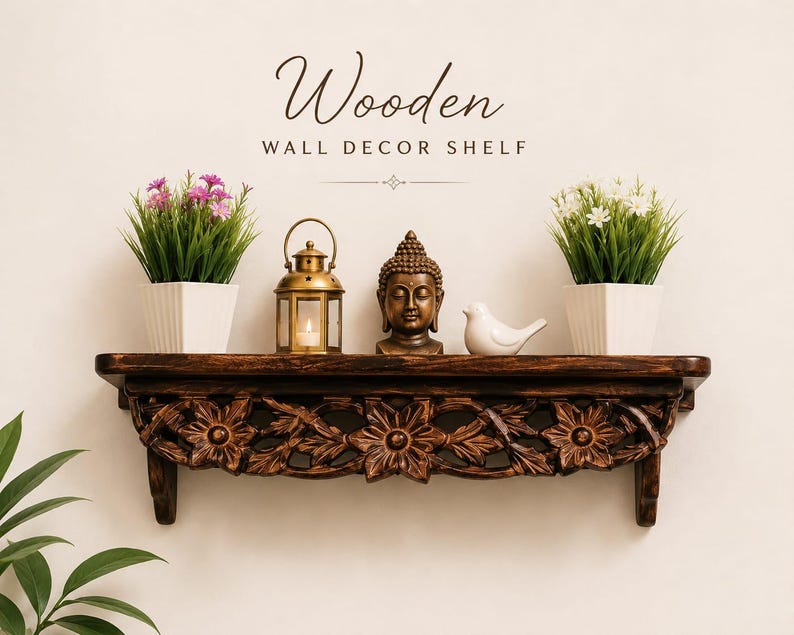 May include: A dark brown wooden wall shelf featuring intricate floral carvings along the front edge. The shelf holds two white square pots with green and pink flowers, a gold metal lantern, a Buddha head statue, and a white bird figurine.