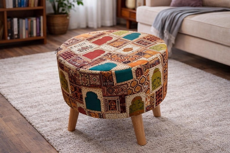May include: A round ottoman with a patchwork design in shades of red, teal, orange, and gold. The upholstered top sits on three wooden legs. This decorative footstool adds a touch of color to any living space.