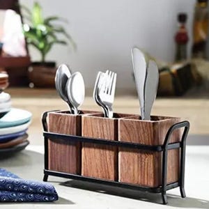 Puede incluir: Un portacubiertos de madera con tres compartimentos, cada uno con cubiertos. El soporte tiene un marco y asas de metal oscuro. La cuberter&iacute;a incluye cucharas, tenedores y un cuchillo. El soporte se encuentra sobre una superficie clara.