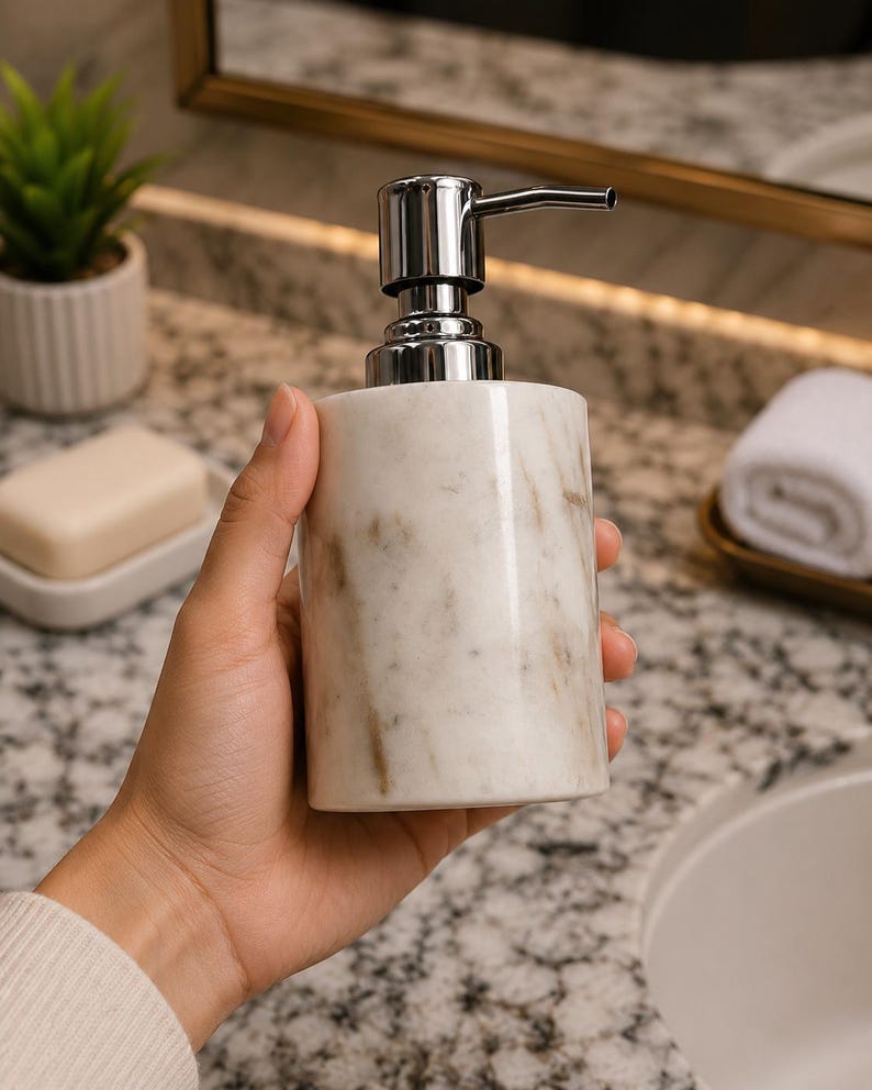 May include: A cylindrical soap dispenser made of white marble with grey veining, featuring a polished chrome pump mechanism at the top. The dispenser has a smooth, polished finish and a sturdy base, designed for dispensing liquid soap or lotion.