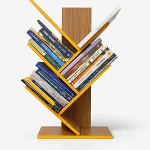 Op de afbeelding: Een moderne, gele boekenplank met een houten achterkant en basis. De schuine planken bevatten een verscheidenheid aan boeken met kleurrijke ruggen. Het ontwerp is eigentijds en ruimtebesparend, geschikt voor een huis of kantoor.