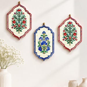 Könnte beinhalten: Drei Wandtafeln mit gewellten Rändern. Die beiden äußeren Tafeln haben rote Ränder und florale Motive mit roten Blüten und grünen Blättern. Die mittlere Tafel hat einen blauen Rand und ein florales Motiv mit blauen Blüten und grünen Blättern.