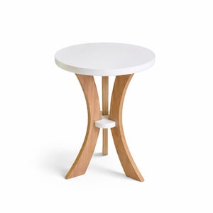 May include: A small, round side table with a white tabletop and a light brown wooden base. The base features curved legs and a small shelf. The table is approximately 61 cm in height and 51 cm in diameter.