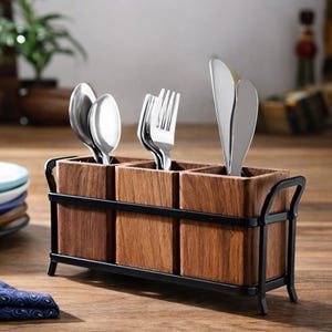 Puede incluir: Un portacubiertos de madera con marco de metal negro, que contiene cubiertos. El soporte tiene tres compartimentos y est&aacute; hecho de madera oscura. Se ven cucharas, tenedores y cuchillos plateados. Est&aacute; sobre una mesa de madera.