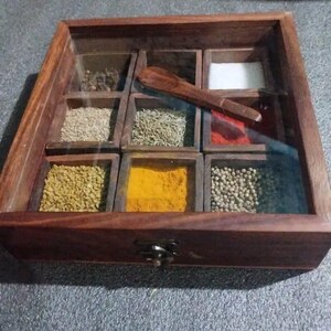 May include: A wooden spice box with a glass lid, featuring nine compartments filled with various spices and a small wooden spoon. The box is made of dark brown wood and has a metal clasp.