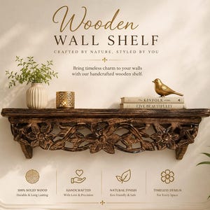 May include: A dark brown wooden wall shelf featuring intricate floral carvings along the front edge. The shelf holds a cream-colored vase with greenery, a gold metallic candle holder, two stacked books, and a small gold bird figurine.
