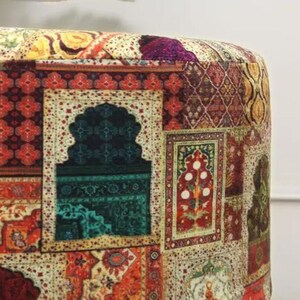 May include: Close-up of a round ottoman with a patchwork design. The fabric features a variety of patterns, including floral, geometric, and traditional rug motifs in shades of red, green, gold, and purple. The ottoman has a soft, cushioned appearance.