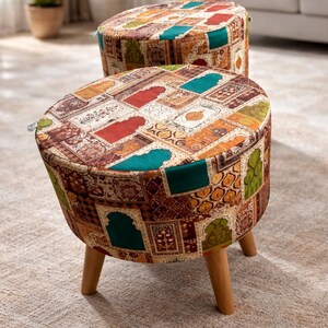 May include: Two round ottomans with a patchwork design in shades of red, green, orange, and brown. The ottomans have wooden legs and are placed on a neutral-colored rug. The fabric has a patterned design.