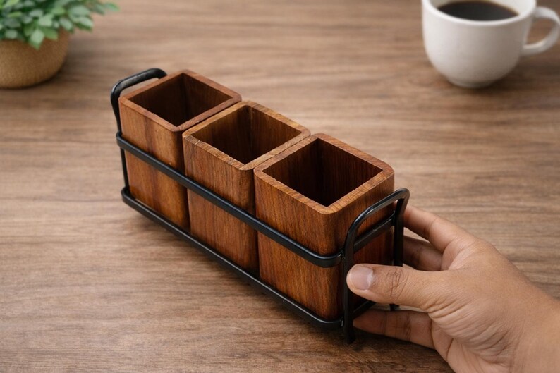 Puede incluir: Un portautensilios de madera con tres compartimentos cuadrados. El soporte est&aacute; hecho de madera de color marr&oacute;n claro y est&aacute; encerrado en un marco de metal negro. El soporte est&aacute; dise&ntilde;ado para colocarse sobre una mesa o encimera.