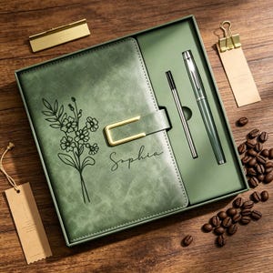 Peut inclure: Un ensemble cadeau comprenant un journal en cuir vert avec un motif floral et le nom "Sophia". Il comprend également un stylo, une recharge et des accessoires dorés.