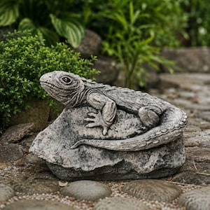 Peut inclure: Une figurine de lézard à la texture de pierre grise posée sur un rocher. Le lézard présente des écailles détaillées, une longue queue enroulée le long de la pierre et des yeux saillants. La sculpture a un aspect réaliste et patiné.