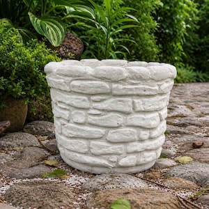 May include: A cylindrical garden planter featuring a textured exterior that mimics the appearance of stacked light gray stones. The planter has a wide, open top and a rounded rim, constructed with a uniform masonry pattern throughout the surface.
