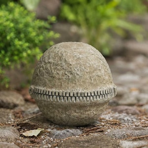 Puede incluir: Una escultura esférica de piedra con una superficie rugosa y texturizada que recuerda a la roca natural. El objeto presenta una banda horizontal prominente alrededor de su centro que imita la apariencia de una cremallera cerrada.