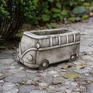 May include: A gray concrete planter shaped like a vintage Volkswagen bus. The planter features a detailed front grille with the Volkswagen logo, round headlights, and a rectangular open top for plants. The exterior has a weathered stone texture.