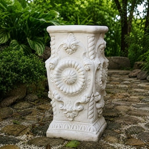 May include: A square off-white garden pedestal featuring ornate relief carvings, including a central circular medallion, rope-style corner columns, and decorative scrollwork on all visible sides, standing on a flat, square base.
