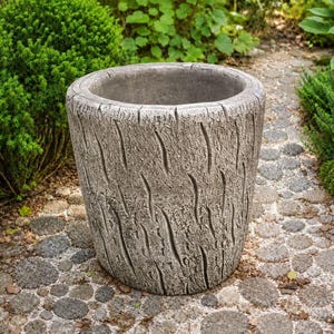 May include: A cylindrical garden planter with a textured grey exterior that mimics the appearance of natural tree bark. The planter features a wide, open top and a deep basin, constructed with a rugged, weathered finish throughout the surface.