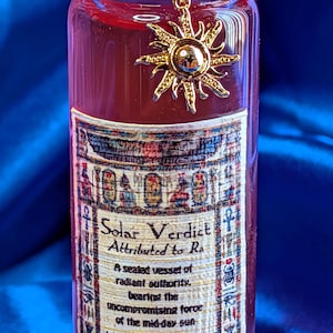 May include: A decorative glass bottle filled with a red liquid, sealed with a red wax cork and a gold sun charm. The label reads "Solar Verdict Attributed to Ra" with additional text. The bottle is a decorative item, not for consumption.