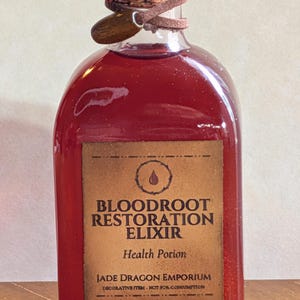 May include: A glass bottle filled with a deep red liquid, labeled "Bloodroot Restoration Elixir." The label is brown with black text and a drop graphic. The bottle is sealed with a cork, brown cord, and red wax.