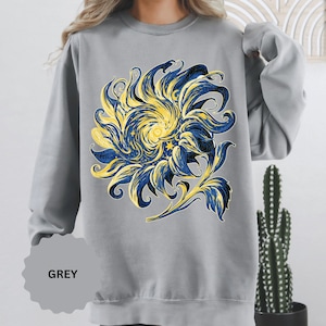 May include: A grey crewneck sweatshirt featuring a large graphic print of a stylized sunflower. The flower petals are rendered in swirling patterns of deep navy blue and vibrant yellow, incorporating small star shapes within the design.