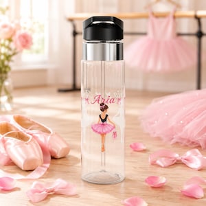 Pode incluir: Uma garrafa de água de plástico transparente com tampa preta e faixa prateada. A garrafa apresenta um gráfico de uma bailarina com tutu rosa e o nome Aria impresso em letra cursiva rosa acima da figura. Um canudo é visível no interior.