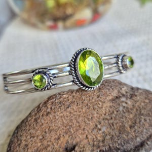 Peut inclure: Un bracelet manchette en argent orné de trois pierres précieuses péridot vert citron serties dans des cadres en métal torsadé. La pierre centrale est ovale et plus grande que les deux petites pierres rondes situées de chaque côté.