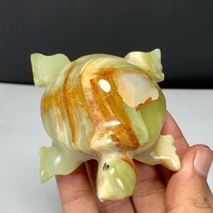 May include: A polished stone turtle figurine carved from light green onyx with prominent bands of orange and white mineral inclusions. The smooth, rounded shell features a glossy finish with visible natural veining and a distinct color gradient.