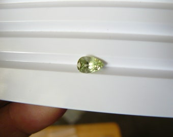 May include: A pear-shaped green gemstone on a white background.