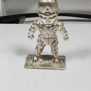 以下が含まれることがあります： 未来的なスーツを着た人の銀色のフィギュア。フィギュアは小さな台座の上に立っています。