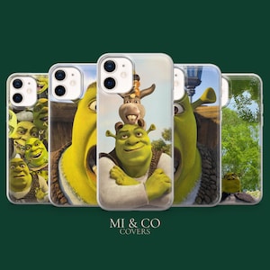 Puede incluir: Una colección de fundas para teléfonos con Shrek y Asno de la película animada. Las fundas muestran imágenes vibrantes de los personajes, con Shrek en varias poses. Las fundas son transparentes con un acabado brillante, y la marca "MI & CO COVERS" está en la parte inferior.