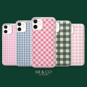 Può includere: Cinque custodie per telefono con motivo a quadretti rosa, blu, verde e bianco. Le custodie sono disposte in fila su uno sfondo verde scuro. Il testo "MI & CO COVERS" è in basso.